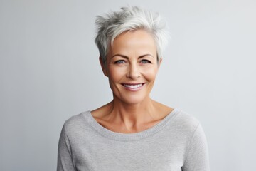 Portrait of a happy mature woman with grey hair standing against grey background