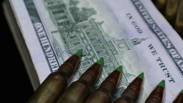 The US Dollar currency notes of 100 denomination, under the rifle bullets with selective focus on them for a cinematic look