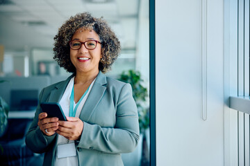 Happy mature businesswoman using cell phone in office and looking at camera.
