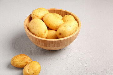 Wooden bowl with raw baby potatoes on grey background