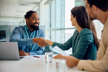 Happy black financial advisor handshaking with his clients during meeting in office. - obrazy, fototapety, plakaty