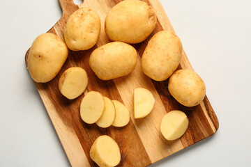 Wooden board with raw baby potatoes on white background