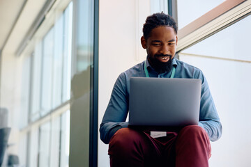 Happy black entrepreneur working on laptop by window in office.