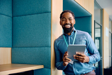 Happy black businessman working on digital tablet in office and looking at camera.