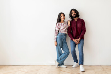 Cheerful beautiful young indian couple posing on white wall background
