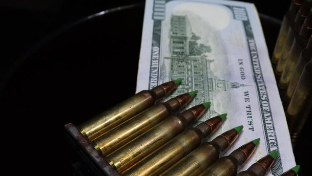 5.56 caliber rifle bullets shining over bank notes of US dollars, a 4K footage for the concept of world super power, influence and American hegemony over other countries and in global politics. 