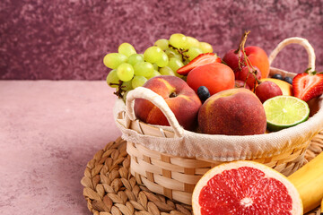 Wicker basket with different fresh fruits on pink table