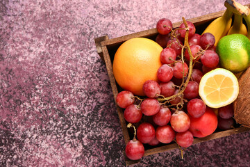 Wooden box with different fresh fruits on purple background