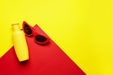 Sunglasses with bottle of sunscreen cream on color background