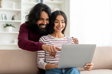 Happy indian couple looking at laptop and choosing purchase