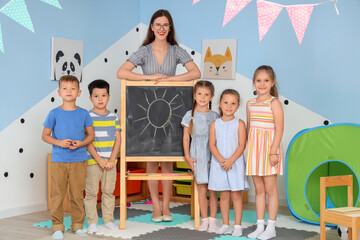 Little children with nursery teacher and chalkboard in kindergarten
