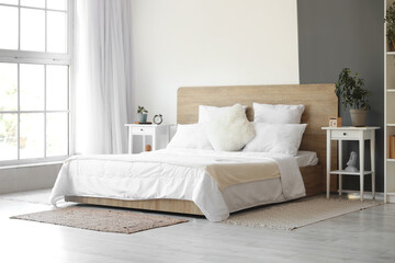 Interior of modern bedroom with white bed and alarm clock on bedside table - obrazy, fototapety, plakaty