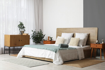 Interior of modern bedroom with wooden bed, houseplants and alarm clock on bedside table - obrazy, fototapety, plakaty