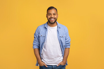 Handsome Black Man With Hands In Pockets Standing On Yellow Studio Background