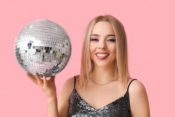 Beautiful young woman with disco ball showing tongue on pink background