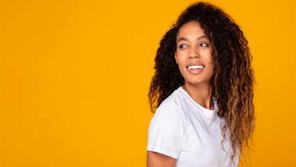 Black lady smiles looking at free space over yellow background