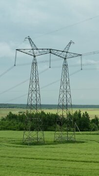 Vertical aerial shot high voltage steel power pylons in green field countryside. Flight over power transmission lines. Electric tower line, daylight, summer day	
