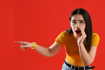 Young gossip woman pointing at something on red background
