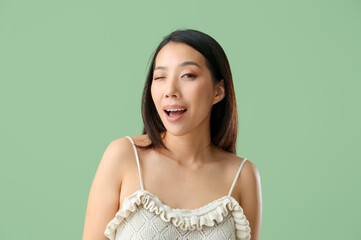 Portrait of pretty young Asian woman winking on green background