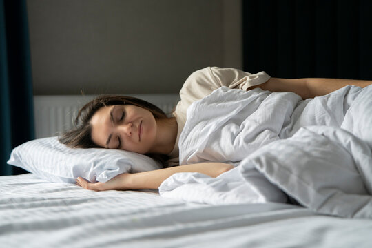 The image captures a young woman as she lies in deep slumber on a cozy bed, embodying a tranquil and restful atmosphere at home.