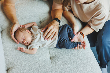 The hands of a loving mother and father hold a newborn baby. Happy parenthood and the joy of being parents - obrazy, fototapety, plakaty