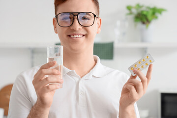 Young man with glass of water and pills at home, closeup