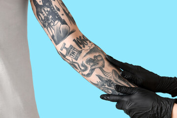 Tattoo master in gloves applying protective film cover over fresh tattoo on man's arm against blue...