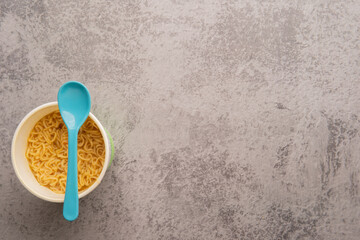 Overhead view of a bowl of instant pasta soup with a spoon light blue on light gray background. Lunch. Fast food concept