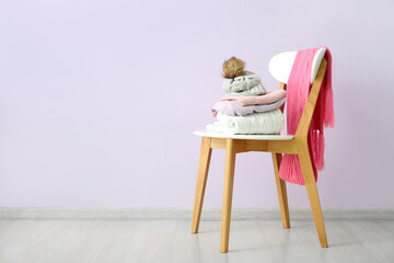 Stacked sweaters with hat and scarf on chair near lilac wall