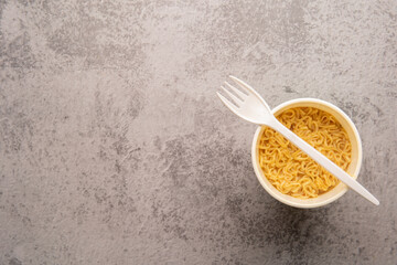 Overhead view of a bowl of instant pasta soup with a plastic fork on a light gray  background. Lunch. Fast food concept