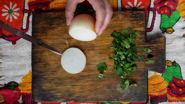 Manos cortando cebolla en tabla de madera para aros de cebolla con perejil.