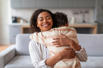 Smiling black mother warmly embracing her preteen son at home