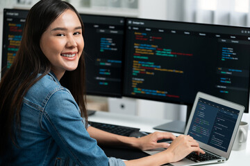 Young Asian in IT developer looking at camera to present with online information on pc with coding program data application, wearing jeans shirt. surround by safety analysis two screens. Stratagem.