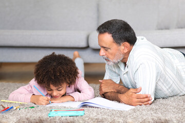 Mature grandfather and grandson kid drawing with colorful pencils indoor