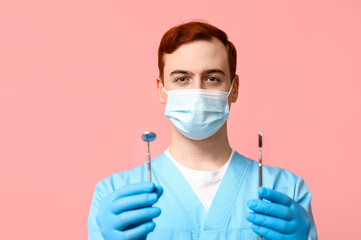 Male dentist in mask with dental tools on pink background. World Dentist Day
