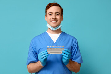 Male dentist with dental shade guide on blue background. World Dentist Day