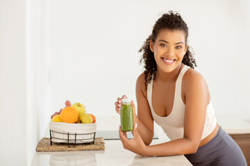 Fit woman in activewear holds smoothie at home kitchen interior