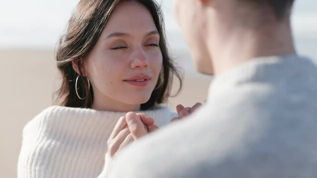 Closeup of a young couple standing at the beach, exchanging affectionate glances, holding hands, and sharing a warm, tender connection