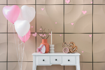 White table with gift box, hearts and heart-shaped balloons near beige wall. Valentine's Day celebration