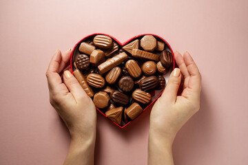 Valentine's Day chocolate candies in red heart shaped box, female hands