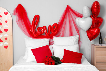 Interior of festive bedroom with bouquet of roses on bed and decorations for Valentine's Day...