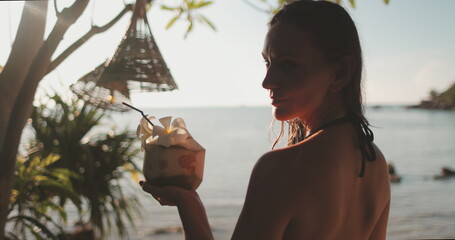 Young girl with coconut cocktail relax on a tropical beach. Palms, ocean, exotic landscape in sunset soft light. Travel, tourism, holiday in Thailand, Koh Phangan.