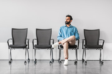 Indian man waiting calmly in office with empty chairs