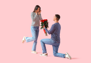Young man proposing to his girlfriend on pink background. Valentine's Day celebration