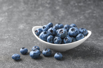 Fresh blueberries in a small round bowl on dark concrete background. Organic berries, healthy food, wild berries.