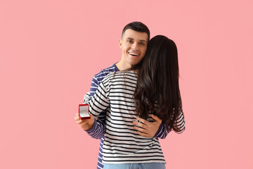 Young engaged couple with wedding ring hugging on pink background. Valentine's Day celebration