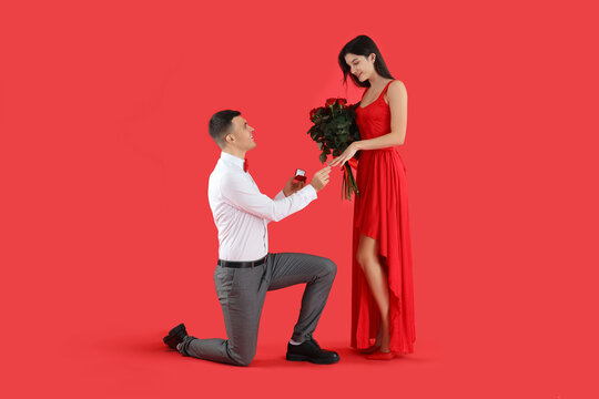 Handsome young man proposing to his girlfriend on red background. Valentine's Day celebration