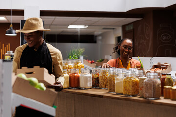 African American business owner and a customer in an eco friendly grocery store, providing fresh food products in reusable packaging. Excellent customer service ensures satisfaction.