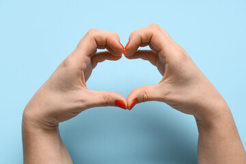 Female hands with red manicure making heart shape on blue background. Valentine's Day celebration