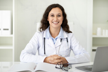 Portrait of beautiful millennial woman doctor sitting at her office - obrazy, fototapety, plakaty
